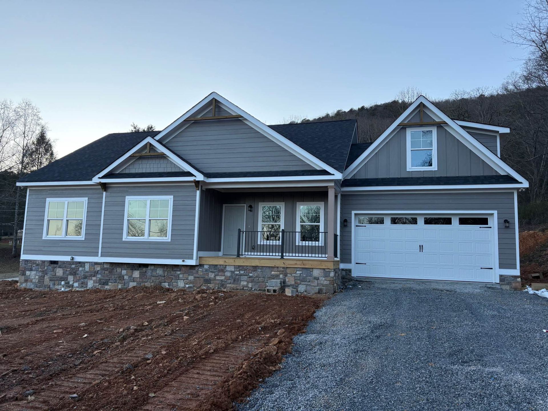 A gray house with a white garage door is sitting on top of a dirt hill.