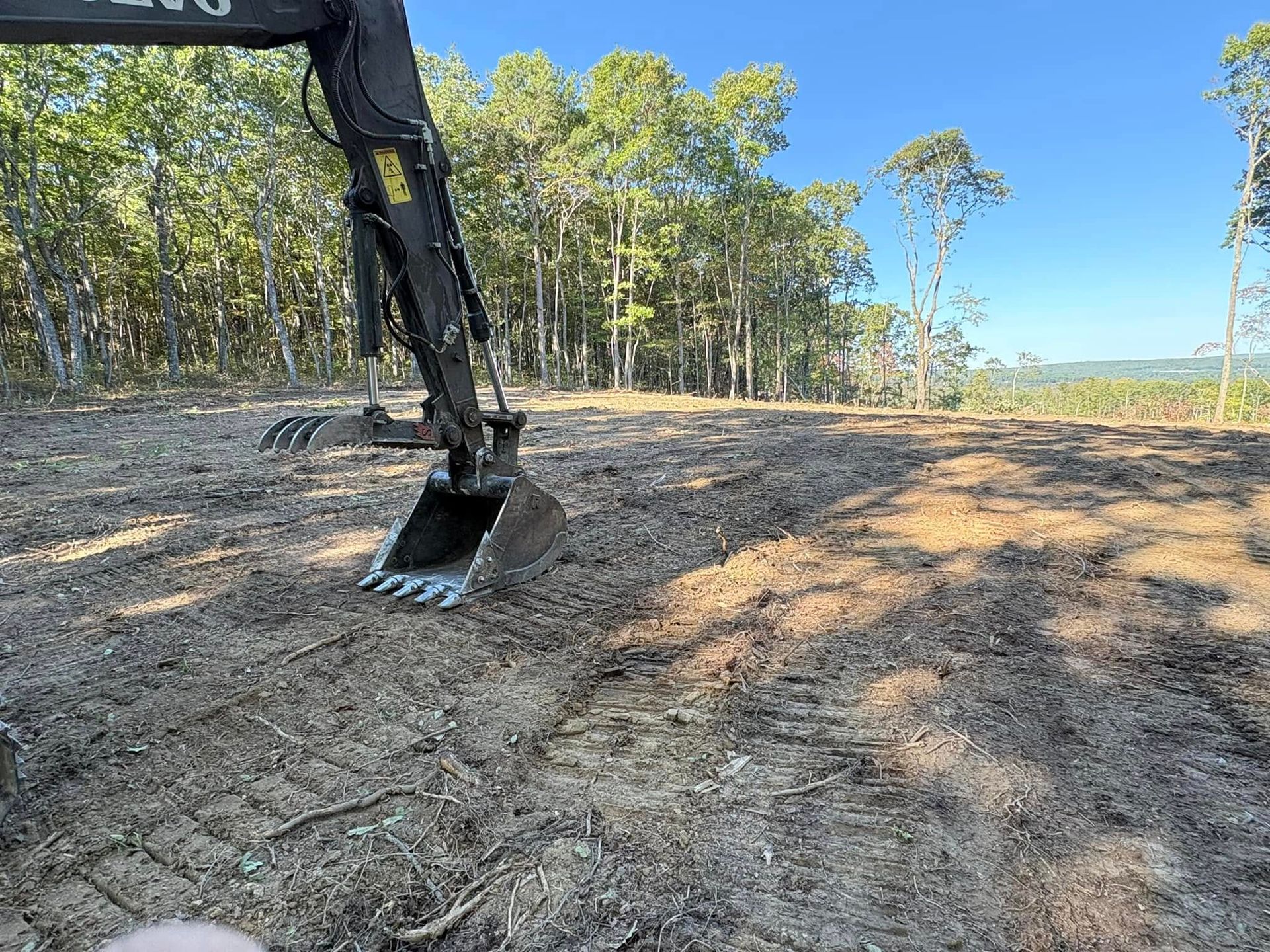 A bulldozer is digging a hole in a field with trees in the background.