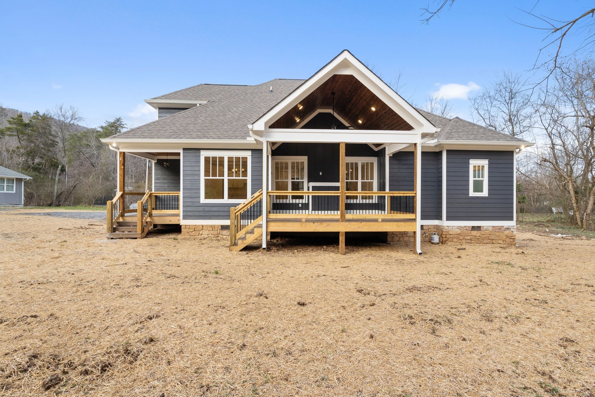 A house with a large porch and stairs is sitting on top of a dirt field.