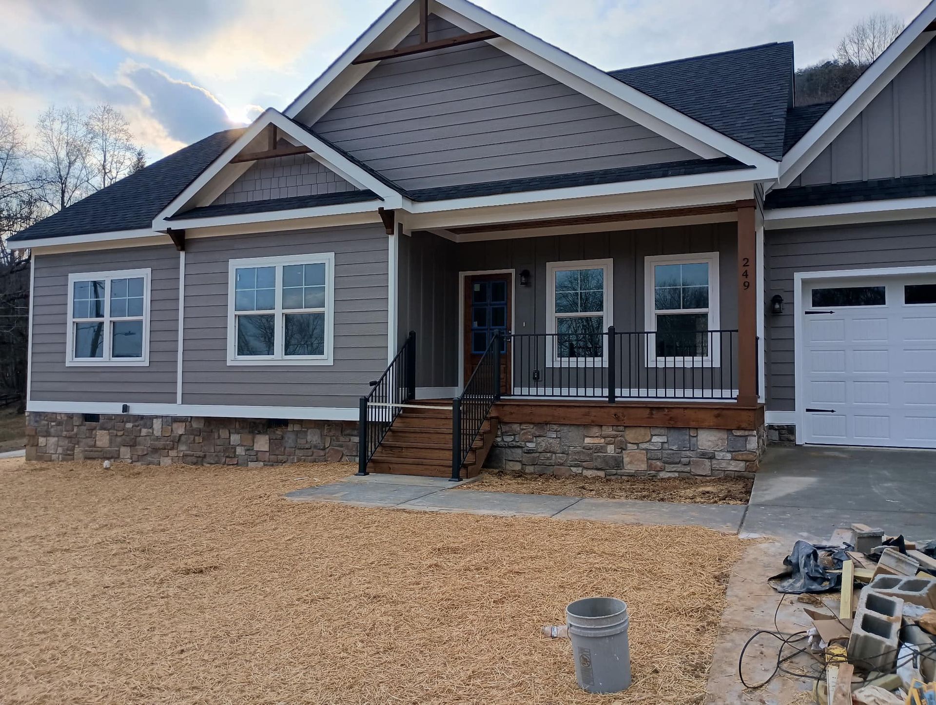 Exterior view of a gray house with stone foundation, porch, and attached garage. Gravel in yard.