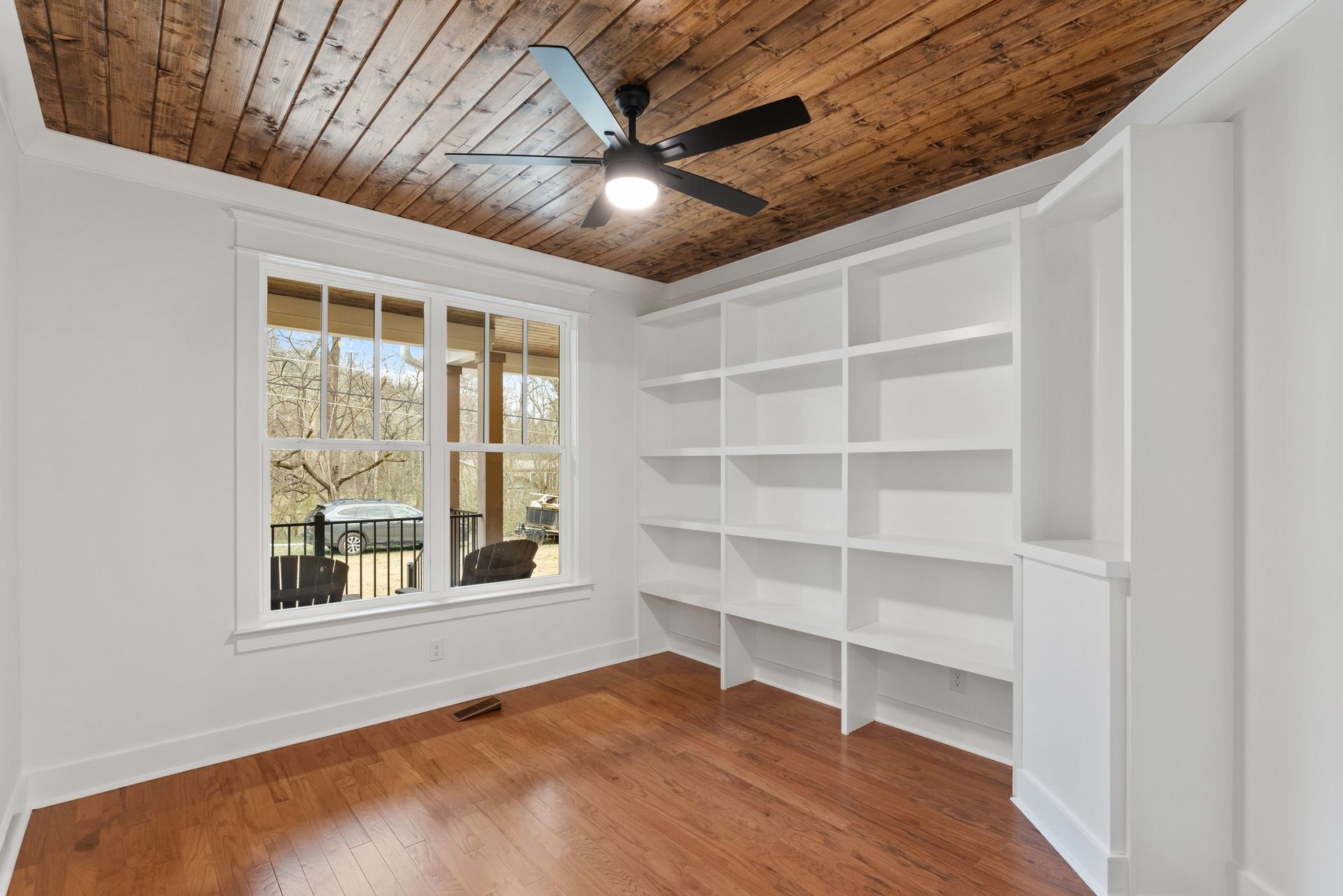 A room with hardwood floors , white shelves and a ceiling fan.