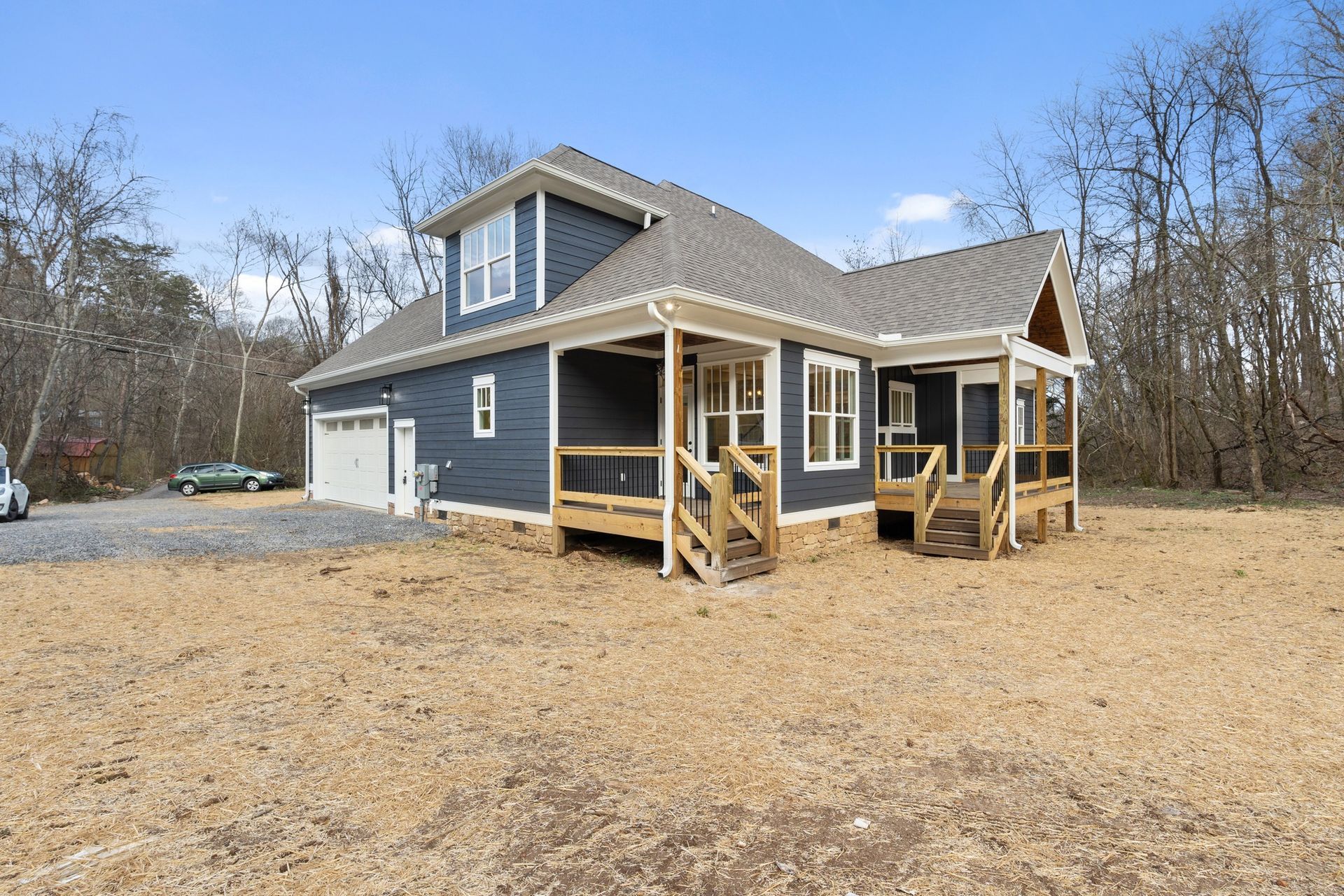 A blue house with a porch and stairs is sitting on top of a dirt field.