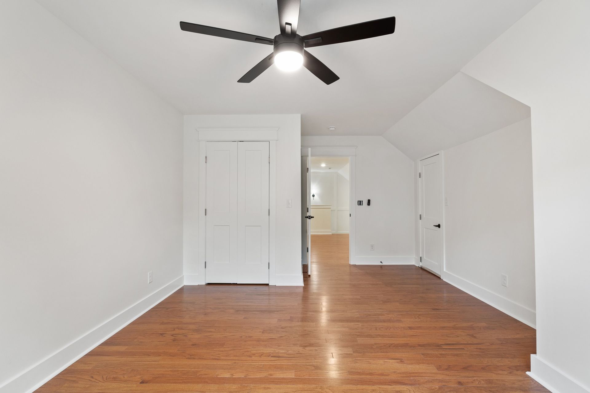 An empty room with hardwood floors and a ceiling fan