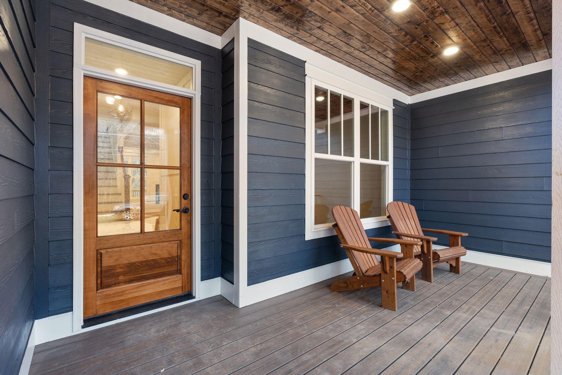 There are two chairs on the porch of a house.