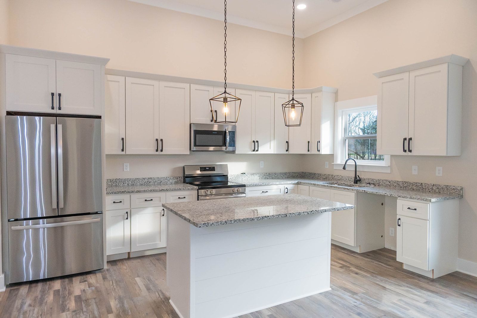 A kitchen with white cabinets , stainless steel appliances , granite counter tops and a large island.