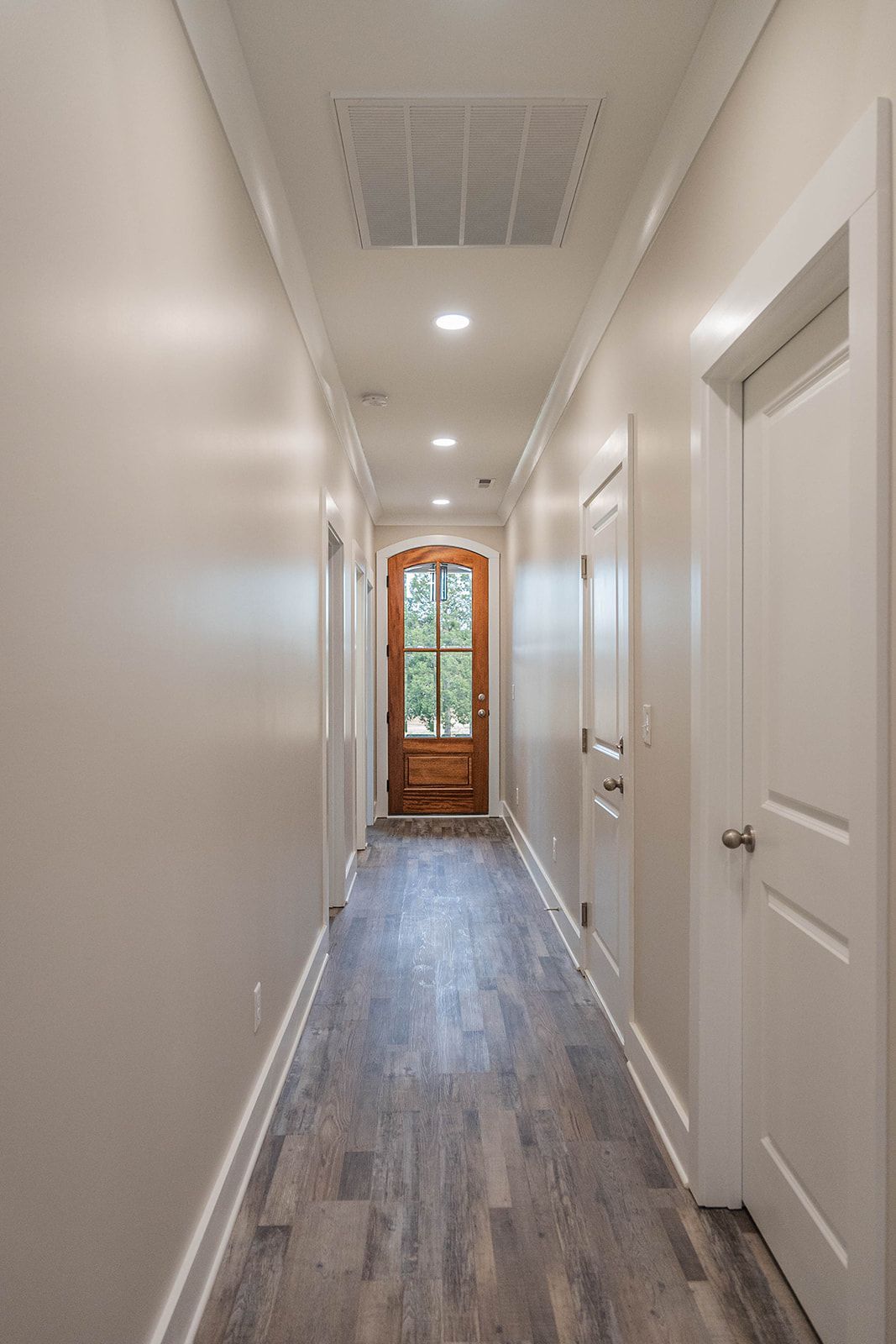 A long hallway with a wooden door and a window in a house.