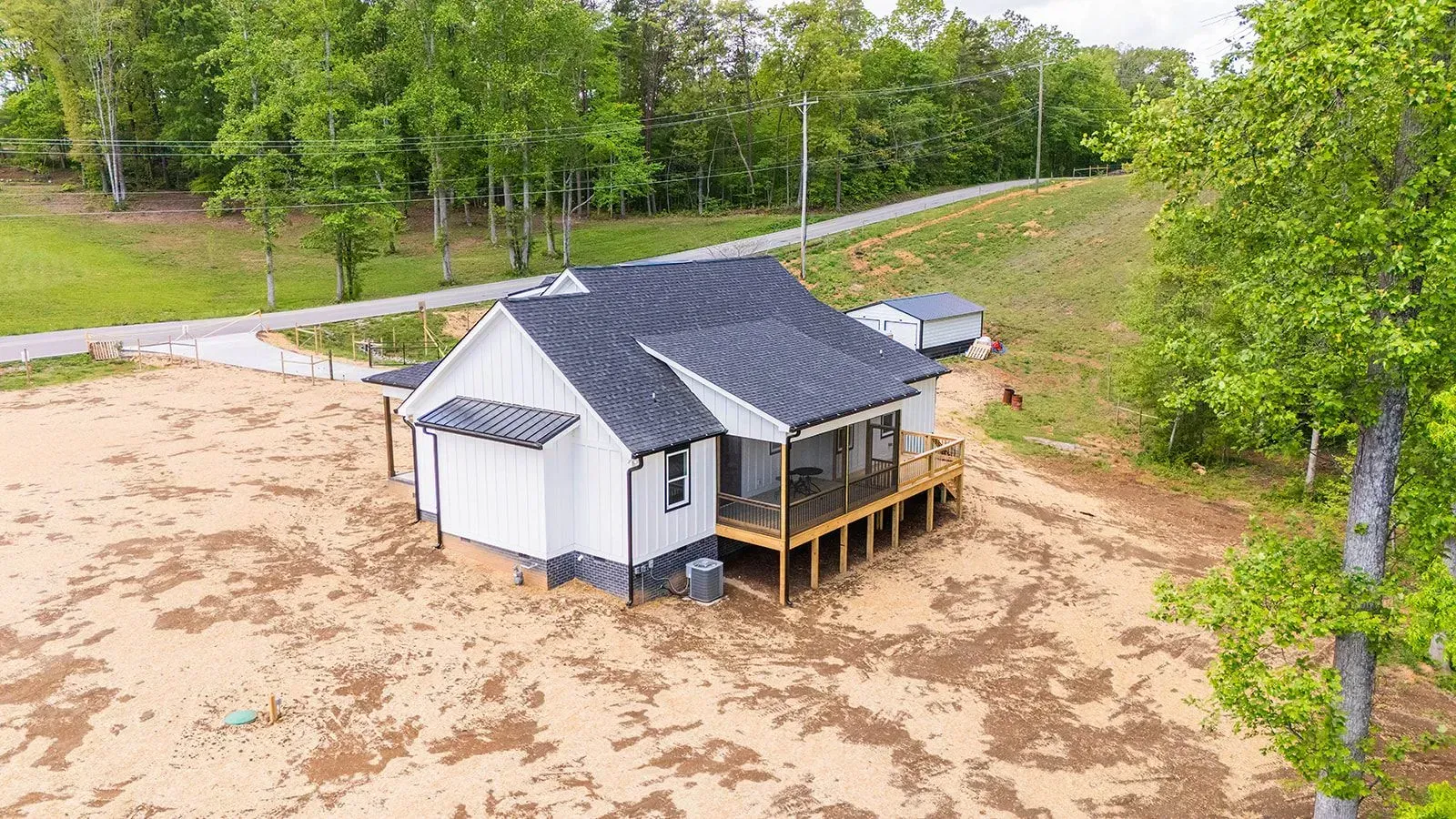 An aerial view of a small white house with a porch in a field surrounded by trees.