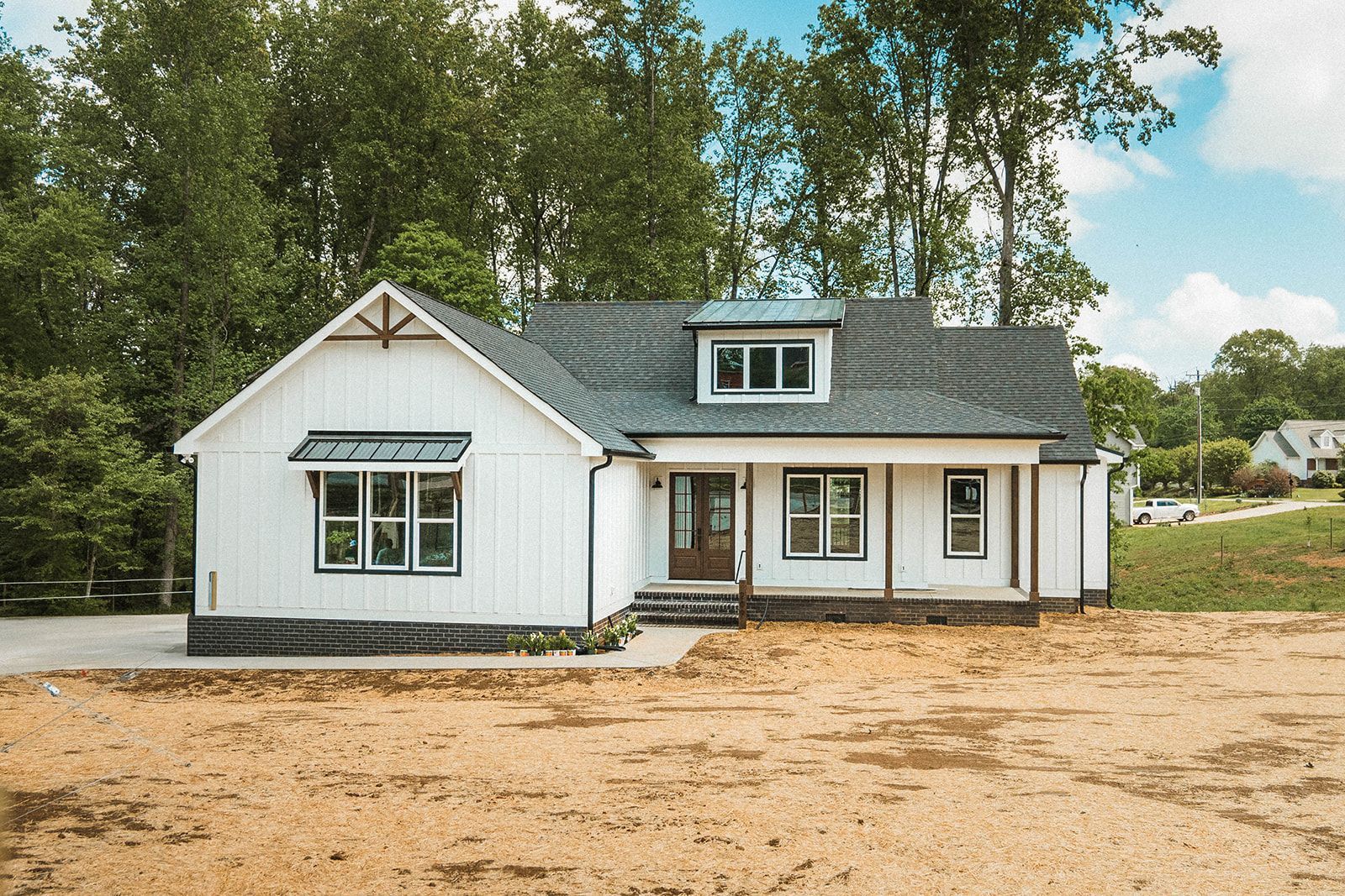 A white house with a black roof is sitting on top of a dirt field.