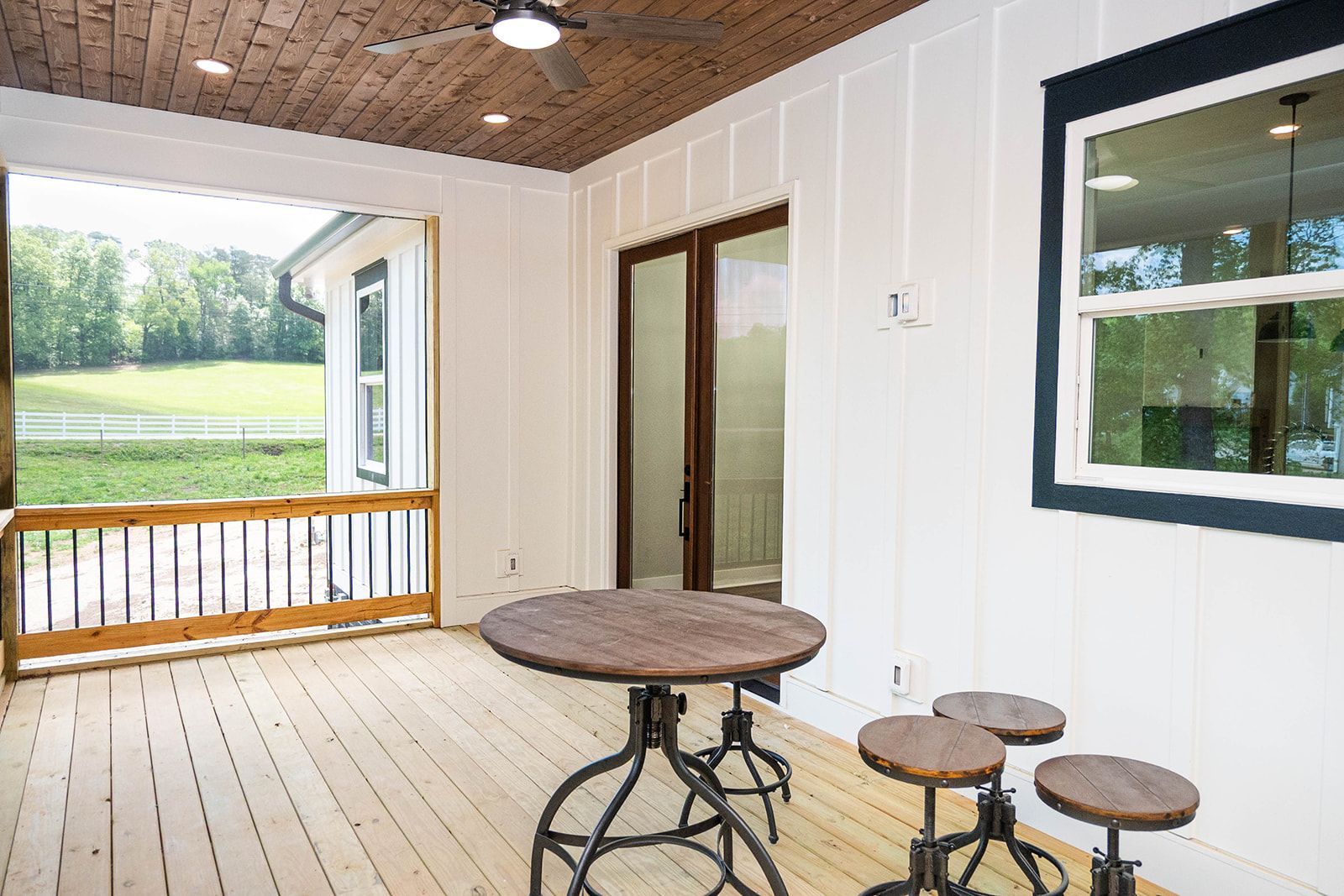 A porch with a table and stools and a ceiling fan.