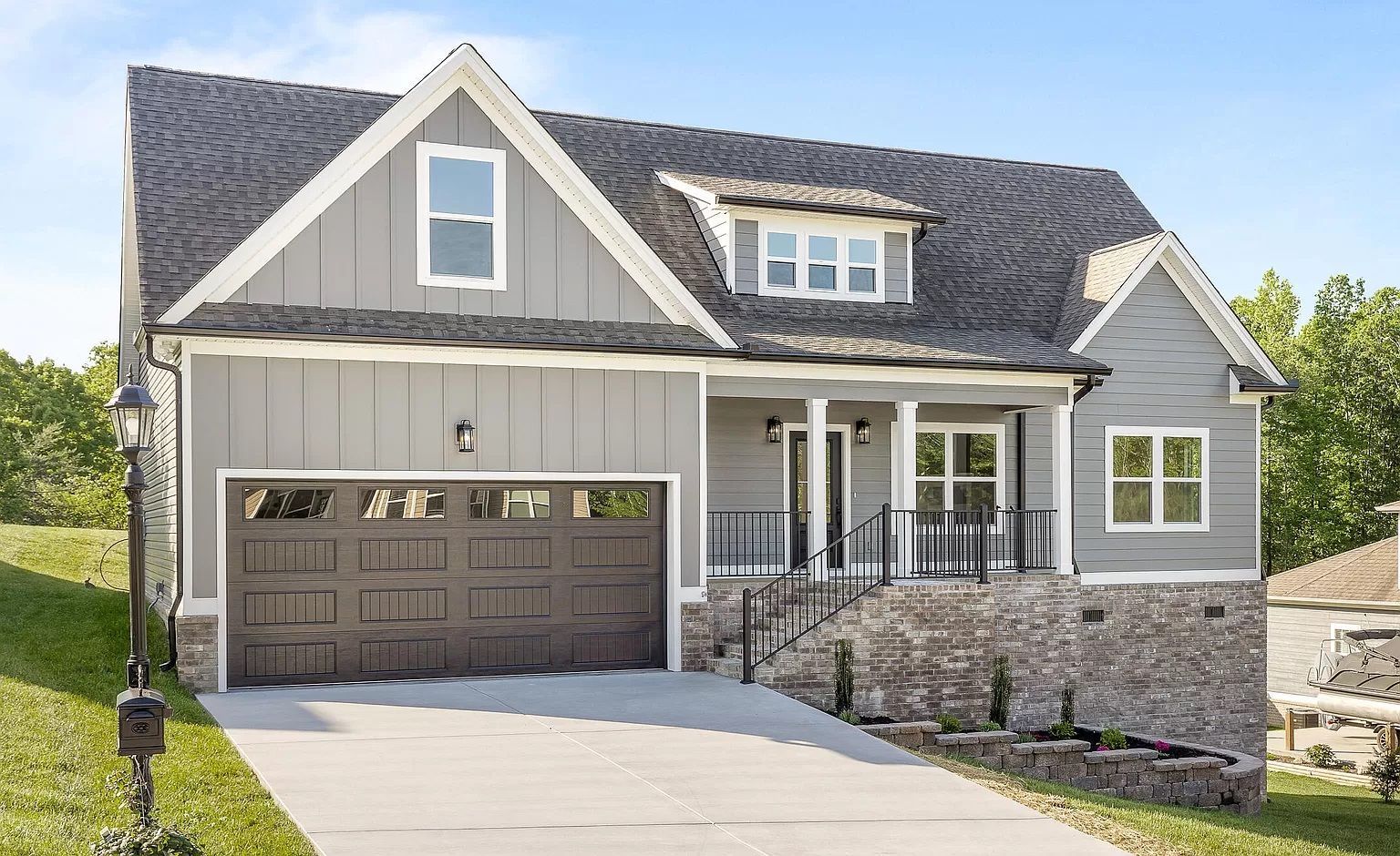 Gray Craftsman-style house with stone accents, a dark garage door, and front porch with steps.