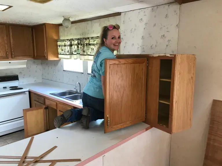 A woman is kneeling down in a kitchen holding a cabinet door.
