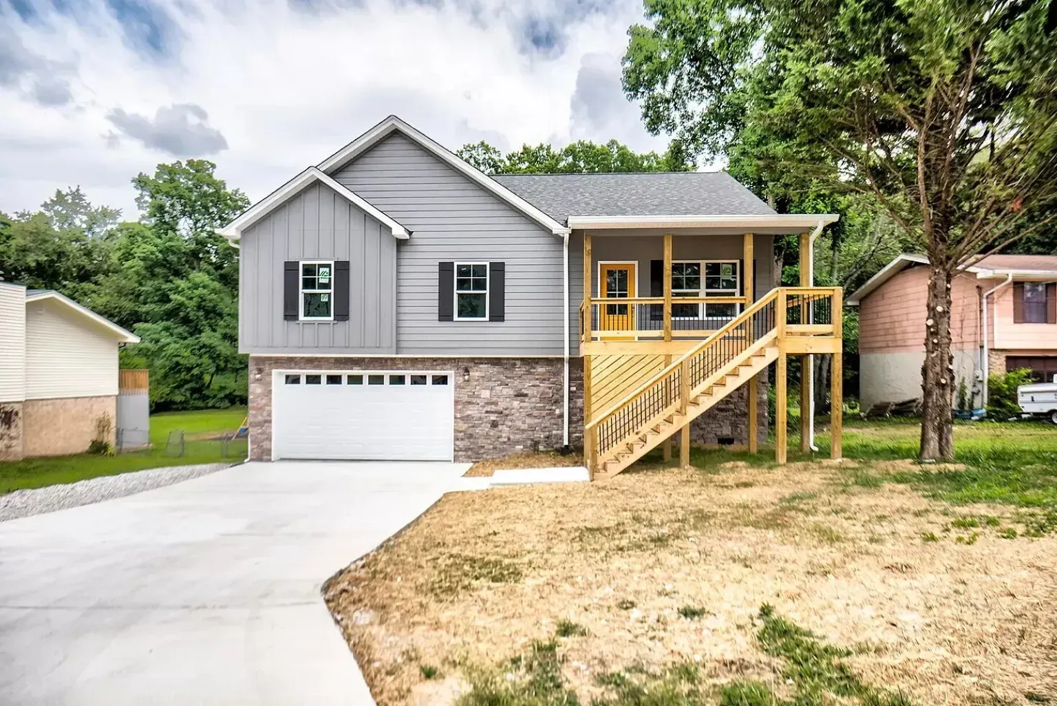 A gray house with a yellow deck and stairs in front of it.
