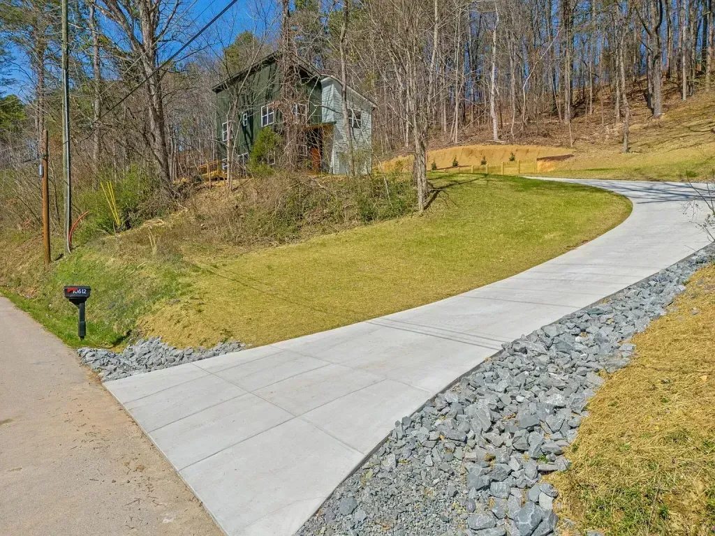 A concrete driveway leading to a house in the woods.
