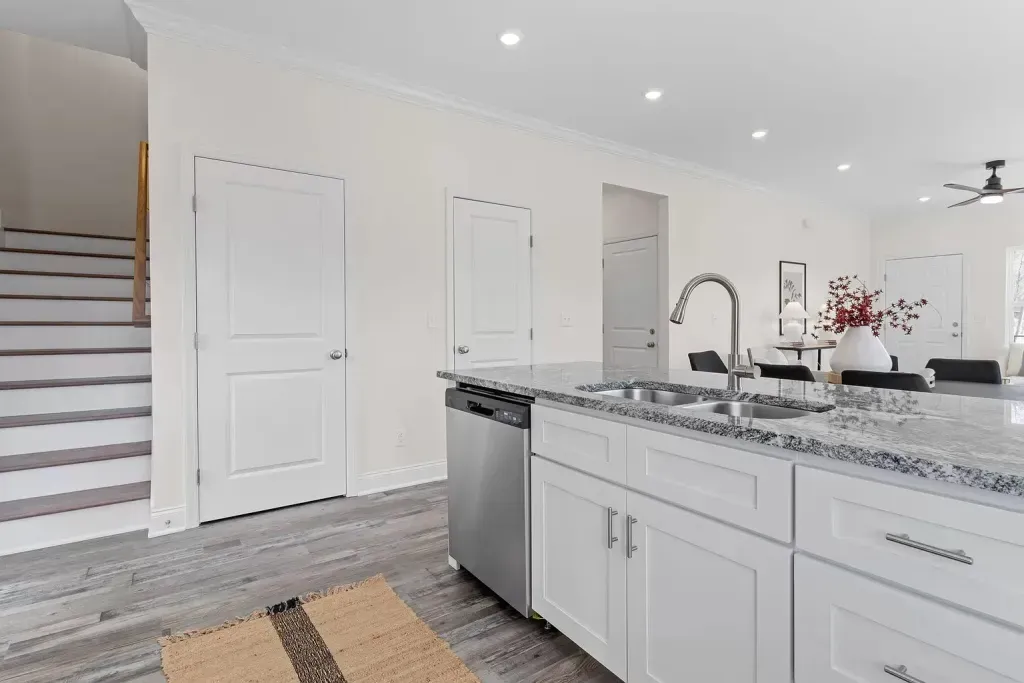 A kitchen with white cabinets , granite counter tops , stainless steel appliances and a rug on the floor.