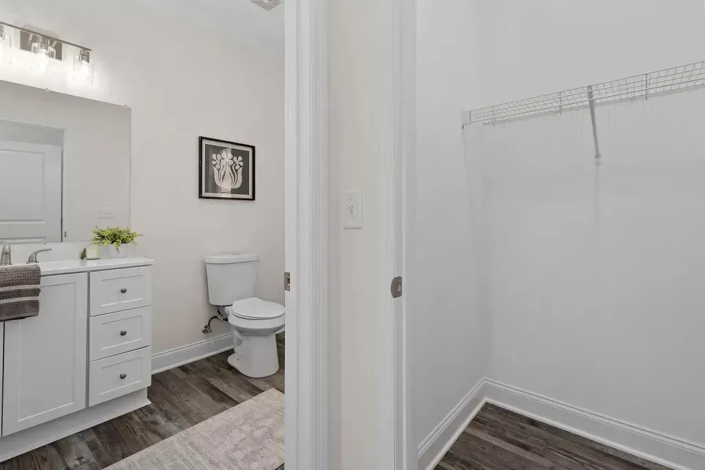 A bathroom with a toilet , sink , mirror and walk in closet.
