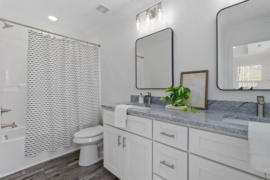 A bathroom with a toilet , sink , mirror and shower.