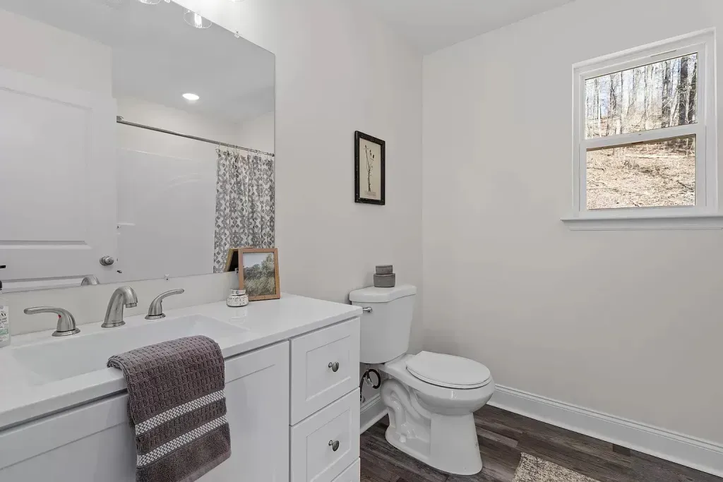 A bathroom with a toilet , sink , mirror and window.