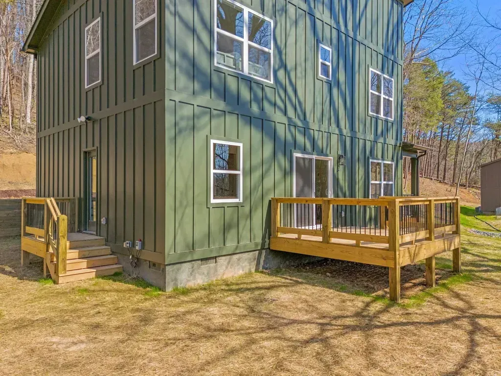 A green house with a wooden deck in front of it.