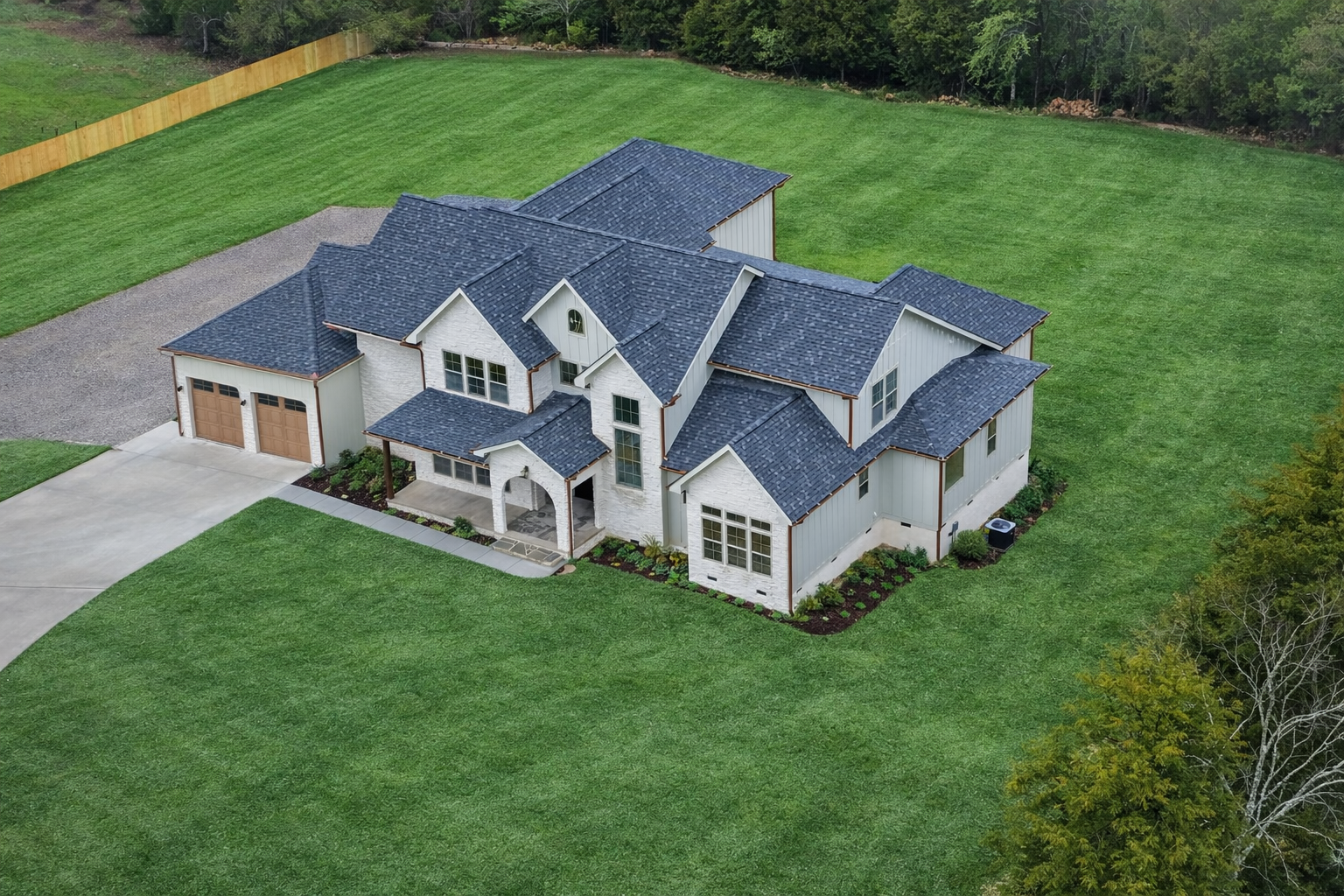 Aerial view of a gray two-story house with a blue roof on a large dirt lot with a driveway.