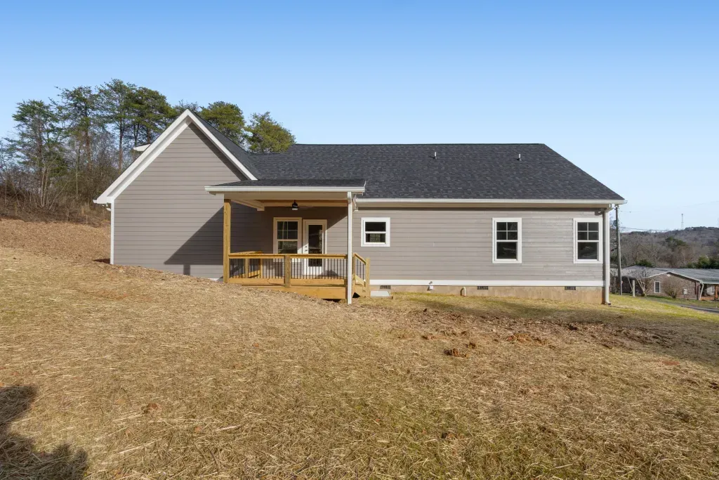 A house with a porch is sitting in the middle of a field.