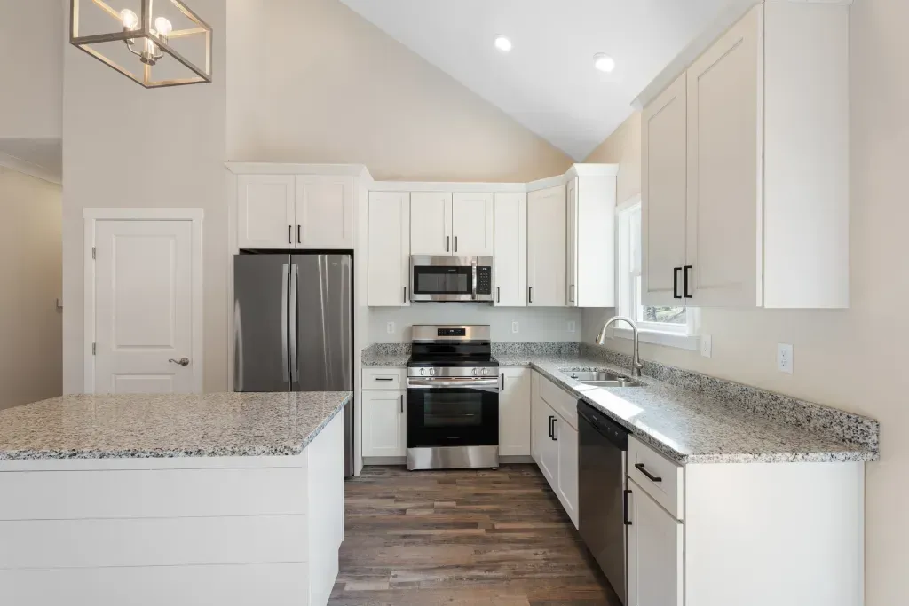 A kitchen with white cabinets , stainless steel appliances , granite counter tops and a large island.