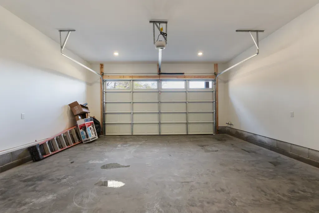 An empty garage with a garage door open and a ladder on the floor.