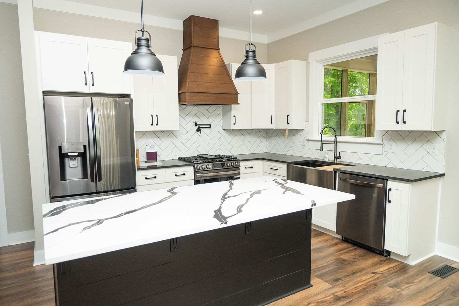 Modern kitchen with white cabinets, marble island, stainless steel appliances, and wood accents.