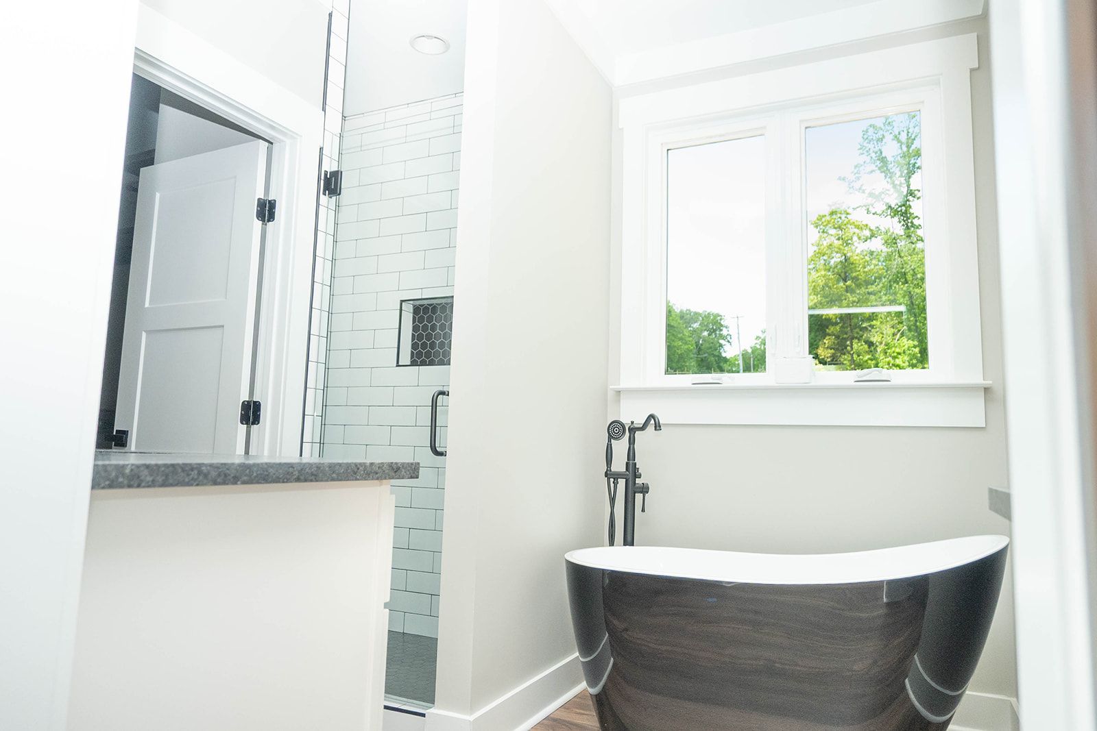Bathroom with a black bathtub by a window, white walls, and a shower visible in the background.