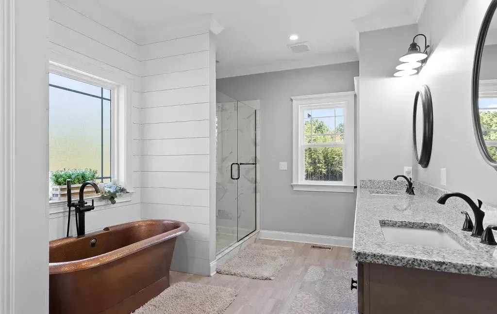A bathroom with a copper tub , sink , mirror and walk in shower.