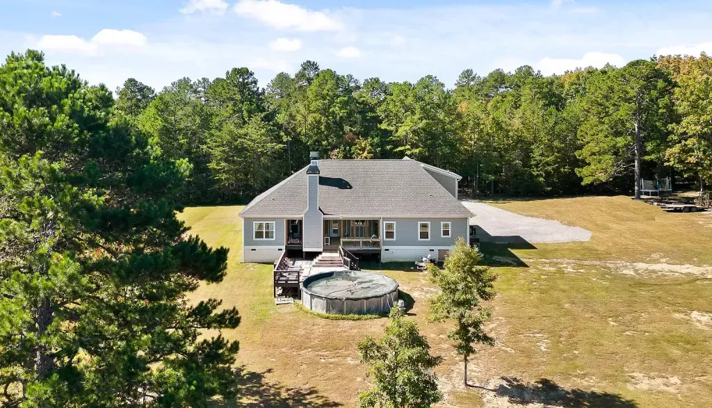 An aerial view of a house in the middle of a field surrounded by trees.