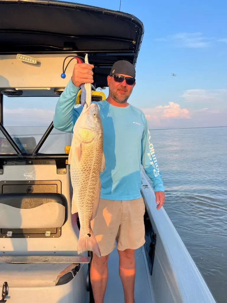 A man is standing on a boat holding a large fish.