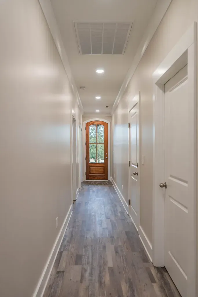 A long hallway with a wooden door and white doors in a house.