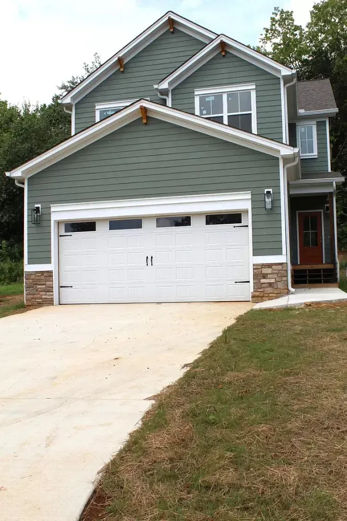 A green house with a white garage door and a driveway