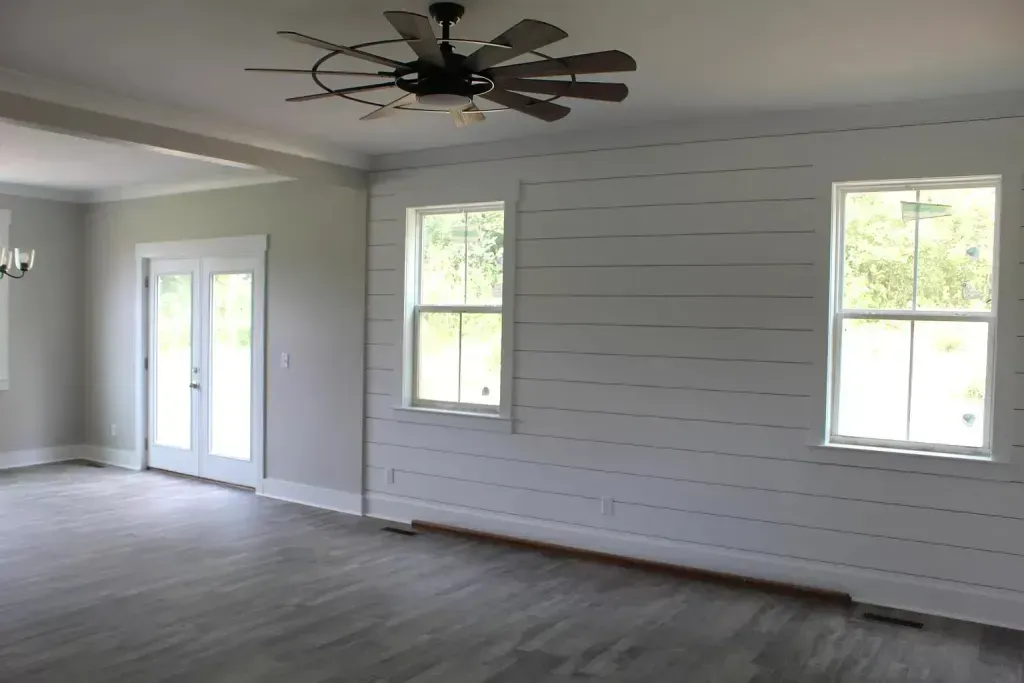 An empty living room with a ceiling fan and three windows.