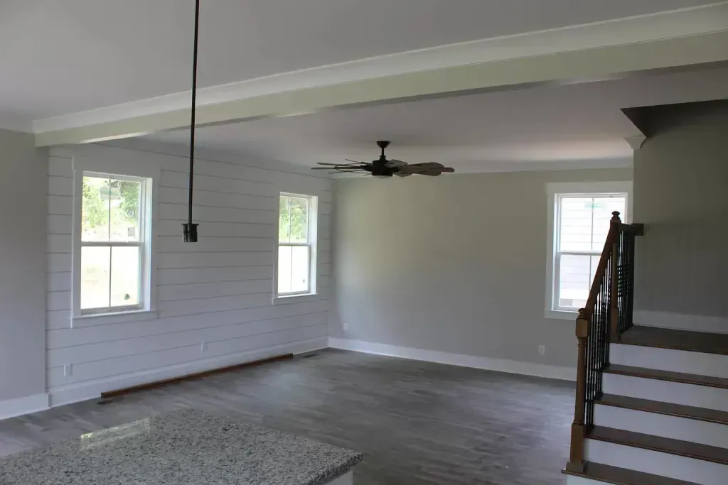 An empty living room with stairs and a ceiling fan
