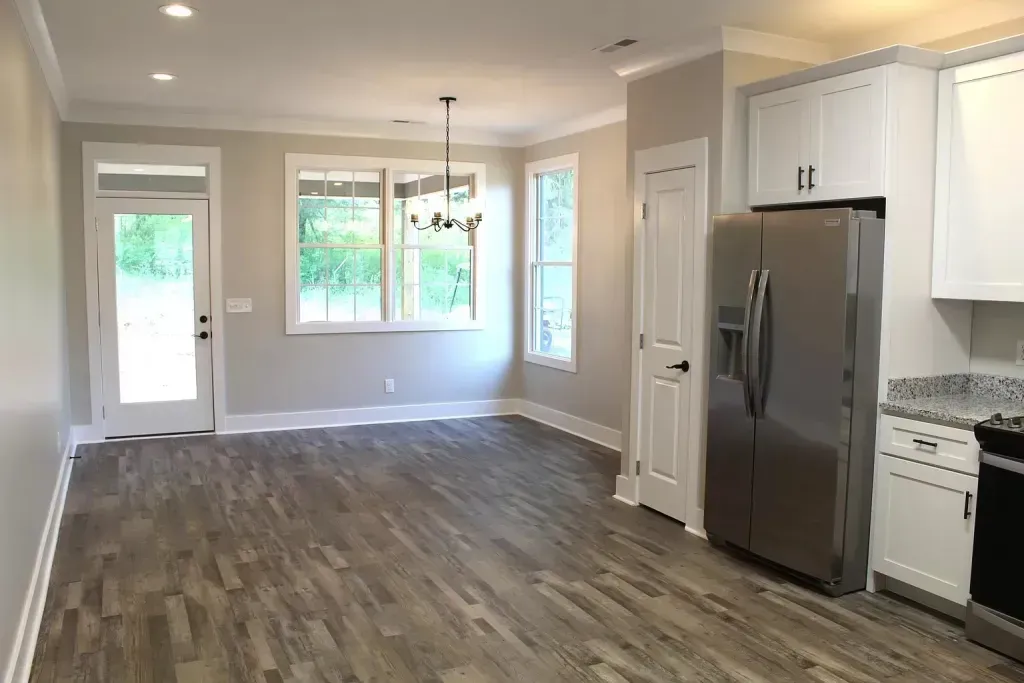 An empty living room with hardwood floors and a stainless steel refrigerator.