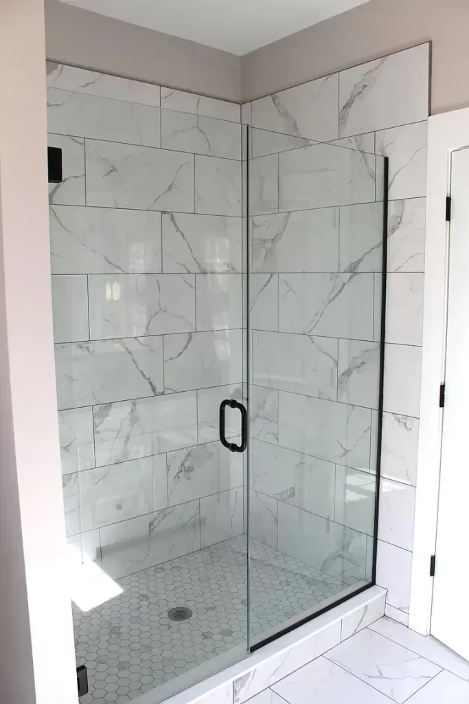 A bathroom with marble tiles and a walk in shower with a glass door.