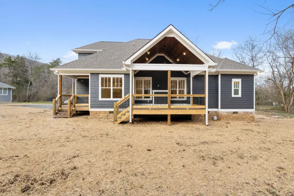 A large house with a large porch is sitting in the middle of a dirt field.