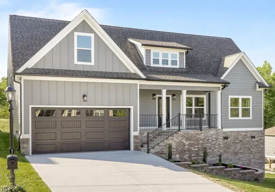 A large gray house with a brown garage door and a driveway.