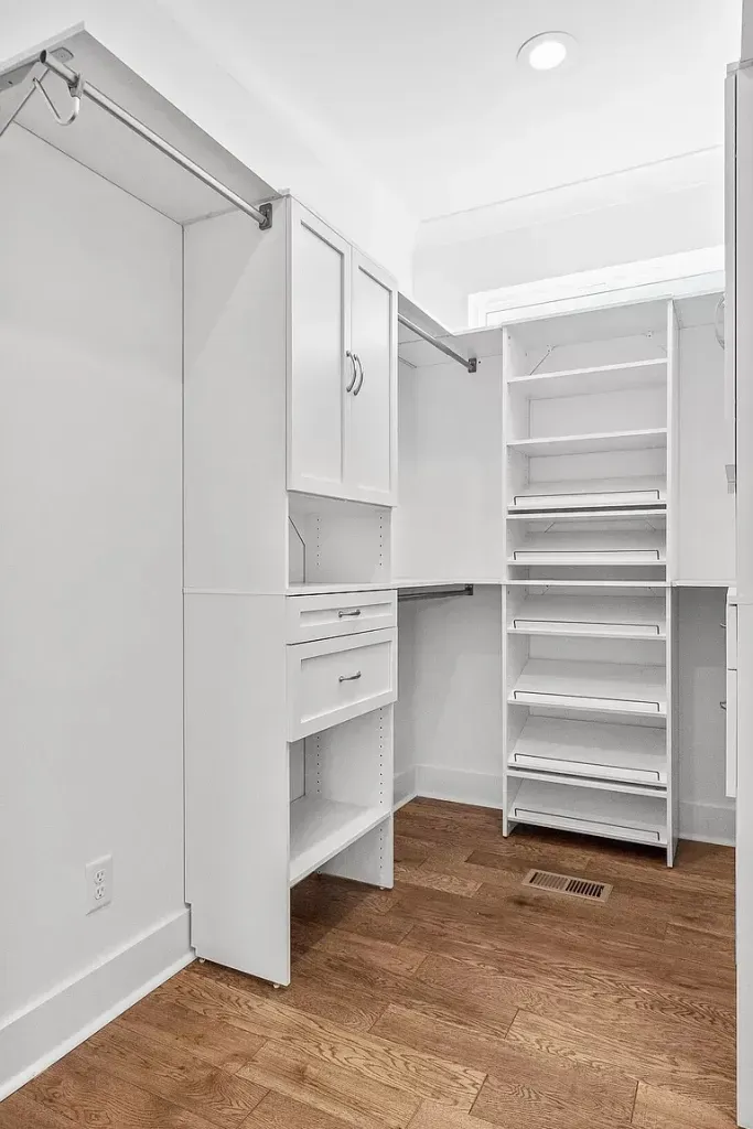 A walk in closet with white shelves and a wooden floor.