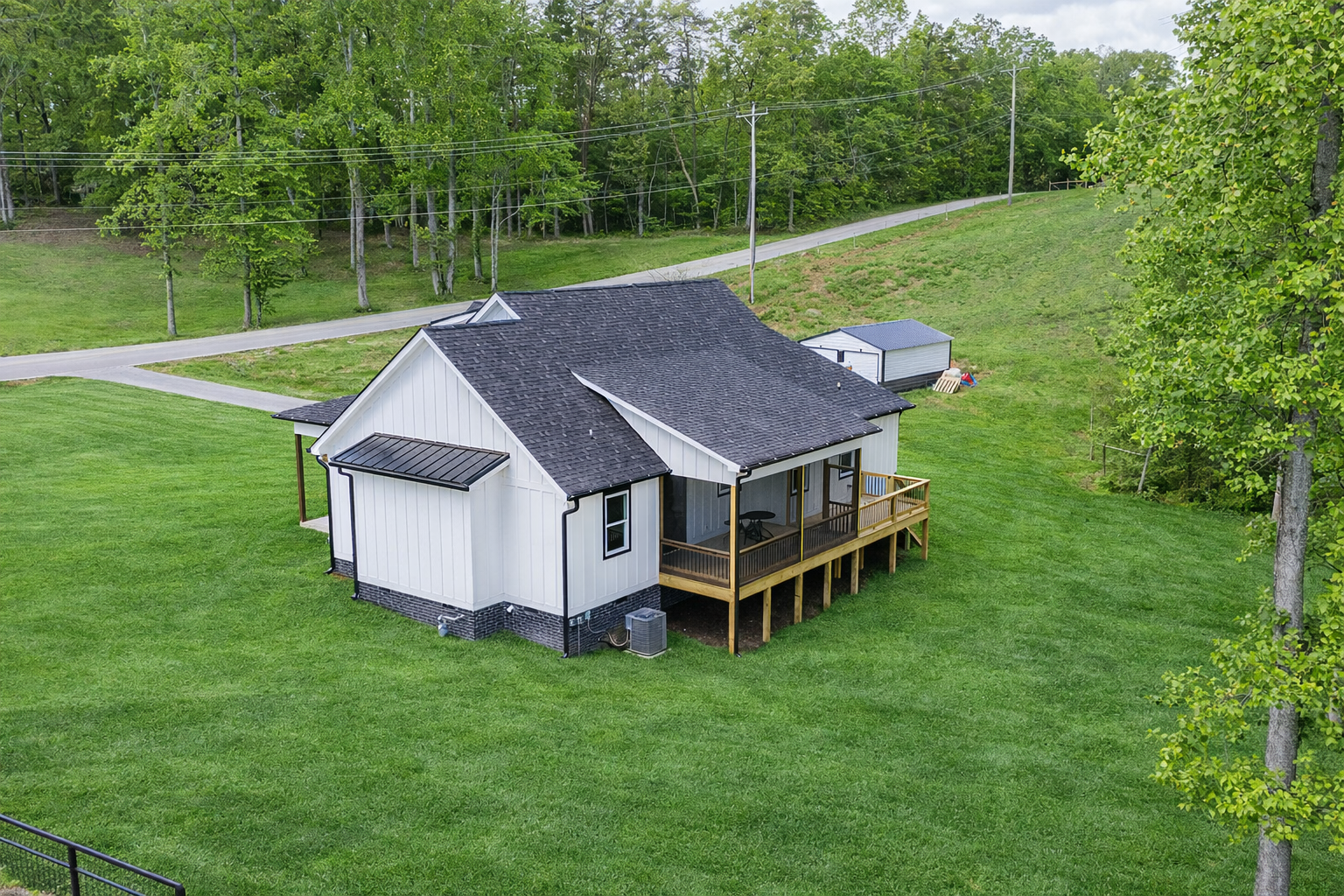 White house with black roof and screened porch on a brown dirt lot, with a green hill in the background.