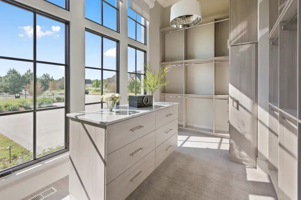 Walk-in closet with large windows, a central island, and built-in shelves, bathed in sunlight.