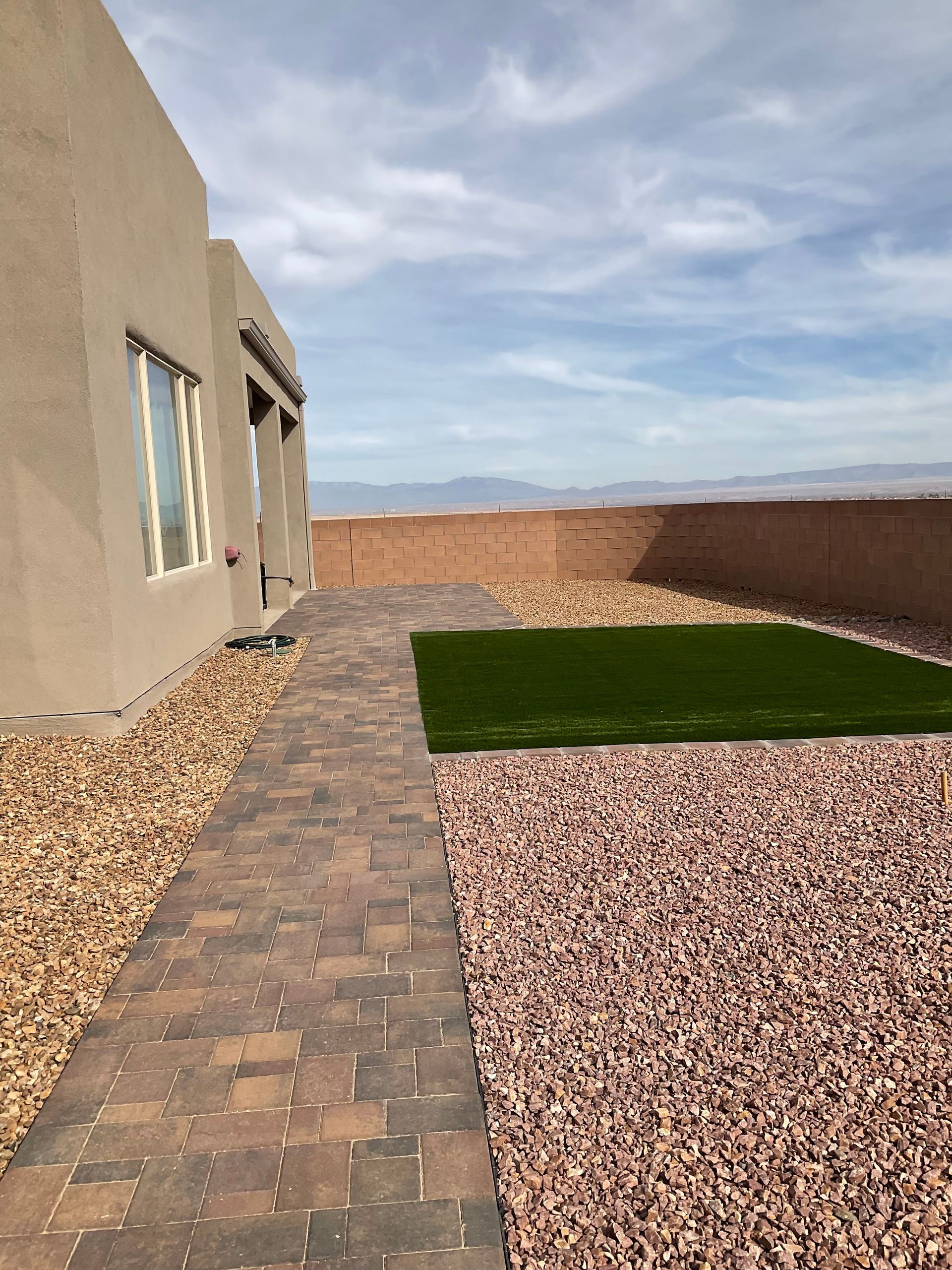 A brick walkway leading to a house with a grassy area in front of it.