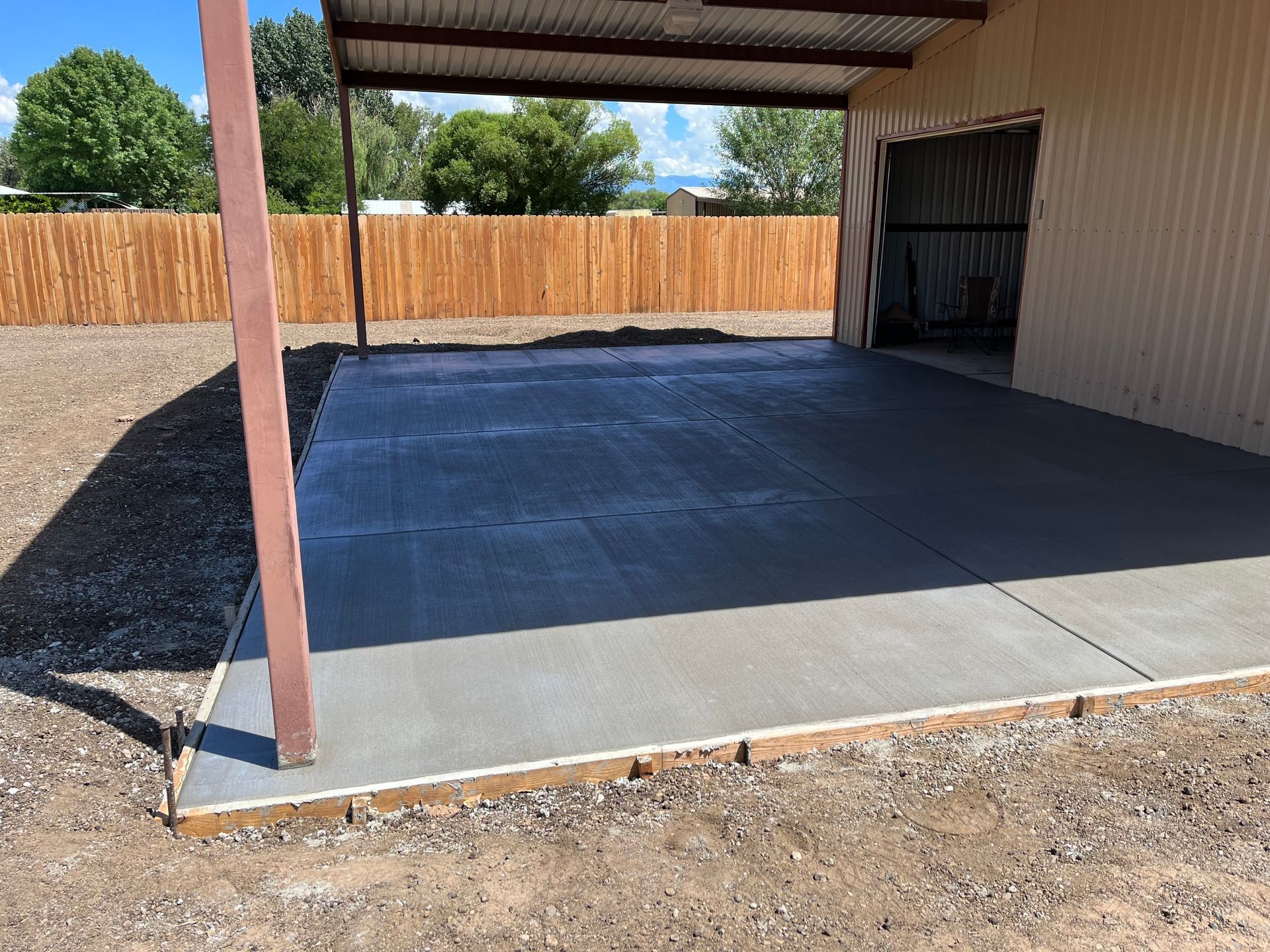 A concrete driveway in front of a garage with a wooden fence in the background.