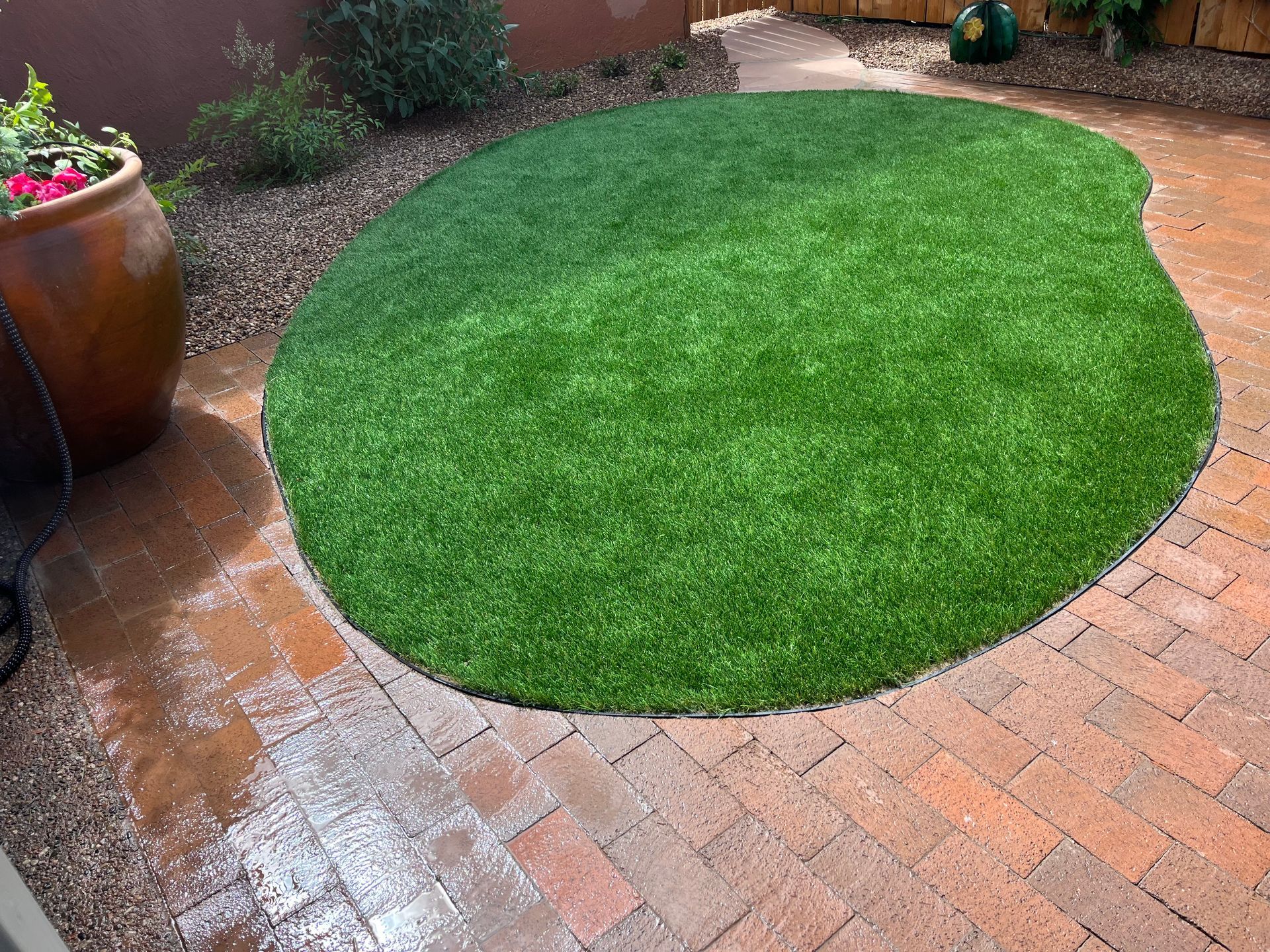 A circle of green grass is on a brick patio.