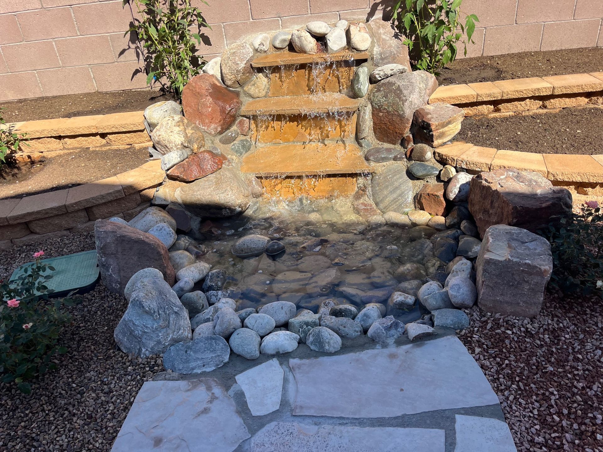 A small waterfall is surrounded by rocks in a backyard.
