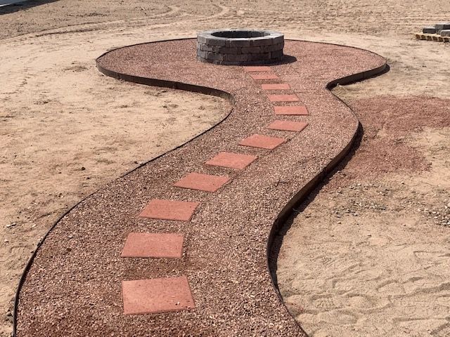 A walkway leading to a fire pit in the middle of a dirt field.