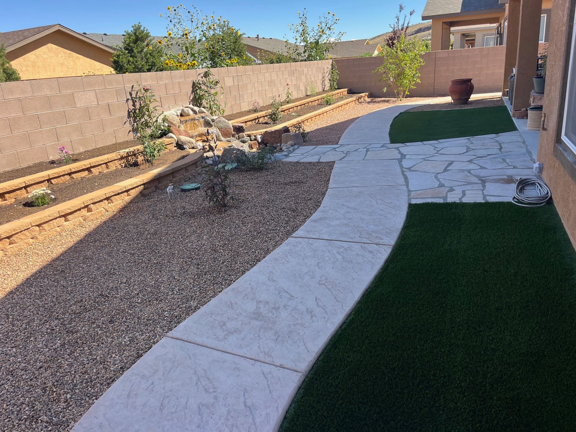 A concrete walkway leading to a backyard with artificial grass and gravel.