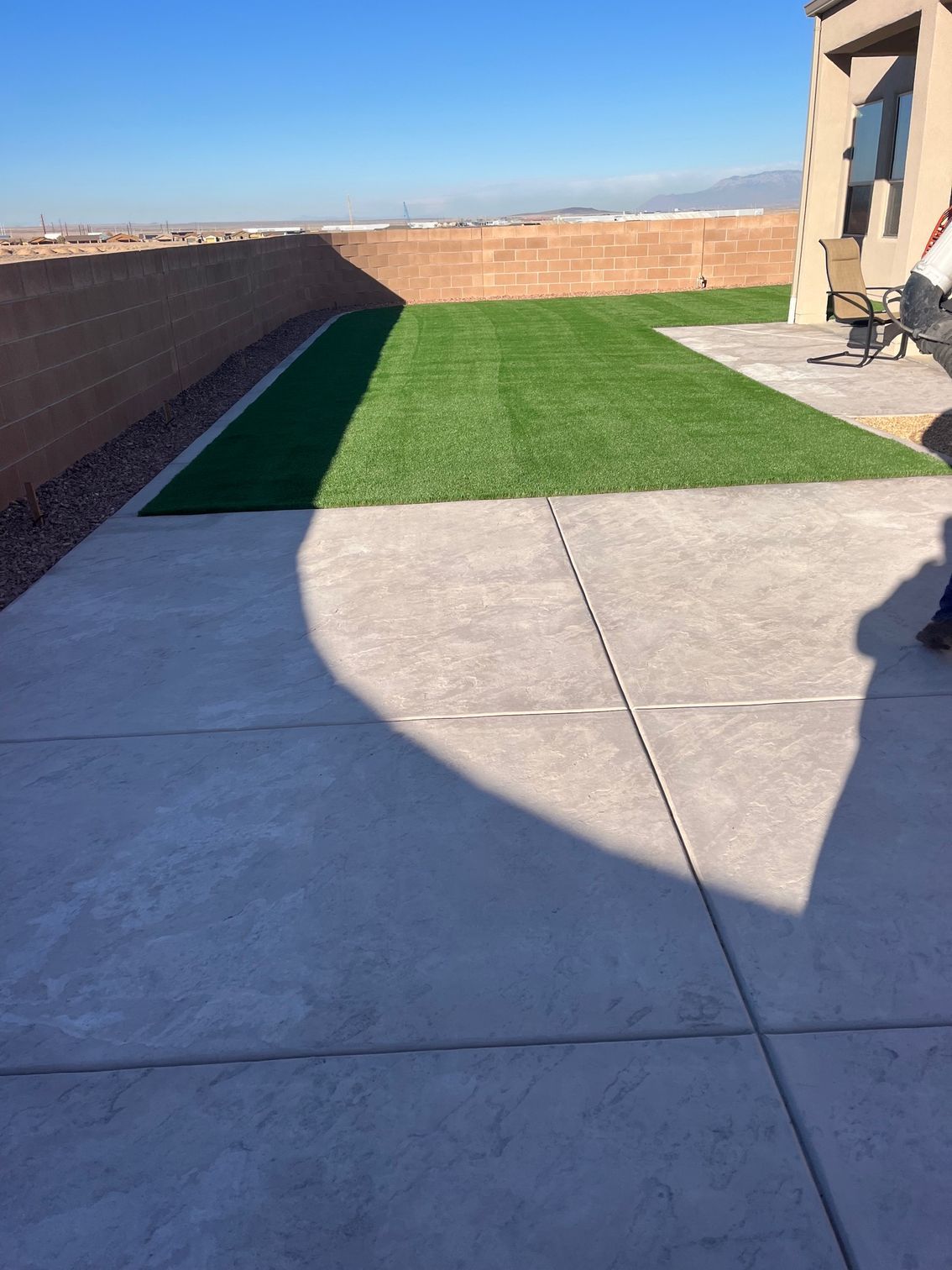 A shadow of a person is cast on a concrete sidewalk in front of a lawn.