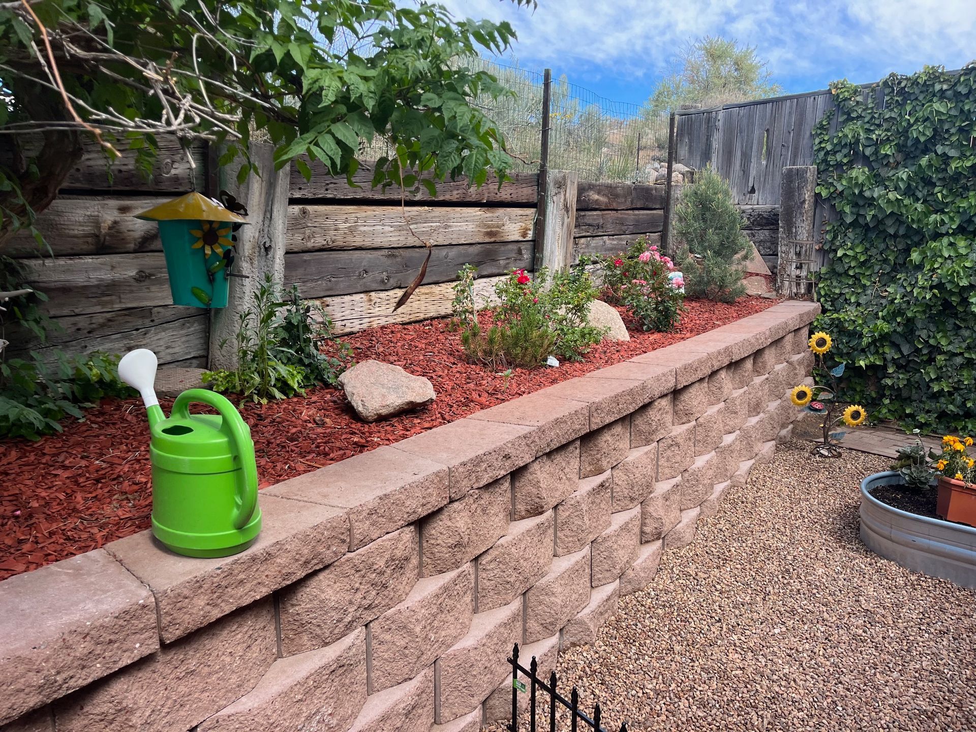 A green watering can is sitting on a brick wall in a garden.